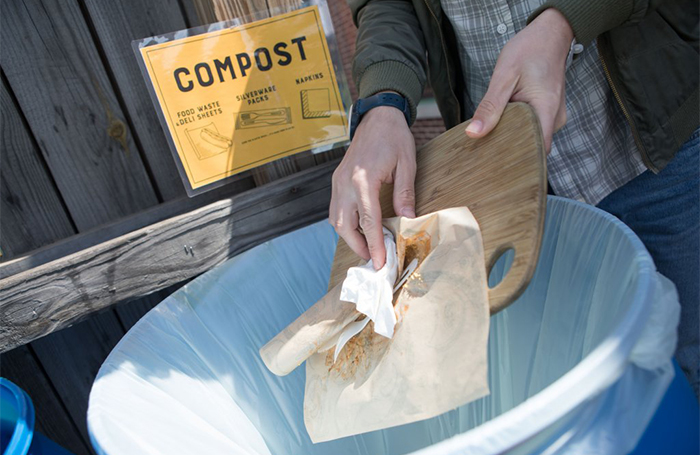 Compostable food is pushed off of a wood platter into a collection bin.