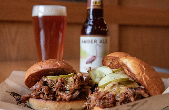 Three pork sliders on a plate, with a bottle and glass of Amber Ale in the background
