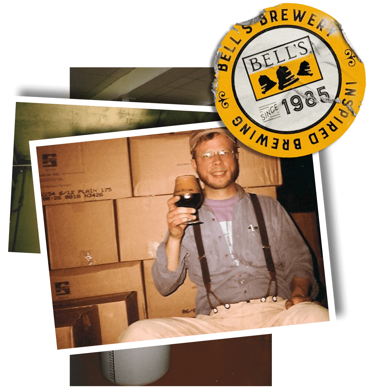 A photo of Larry Bell sitting on cardboard boxes holding a snifter glass full of Amber Ale