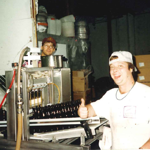 a vintage photo of two lads smiling next to a bottling machine from beer history