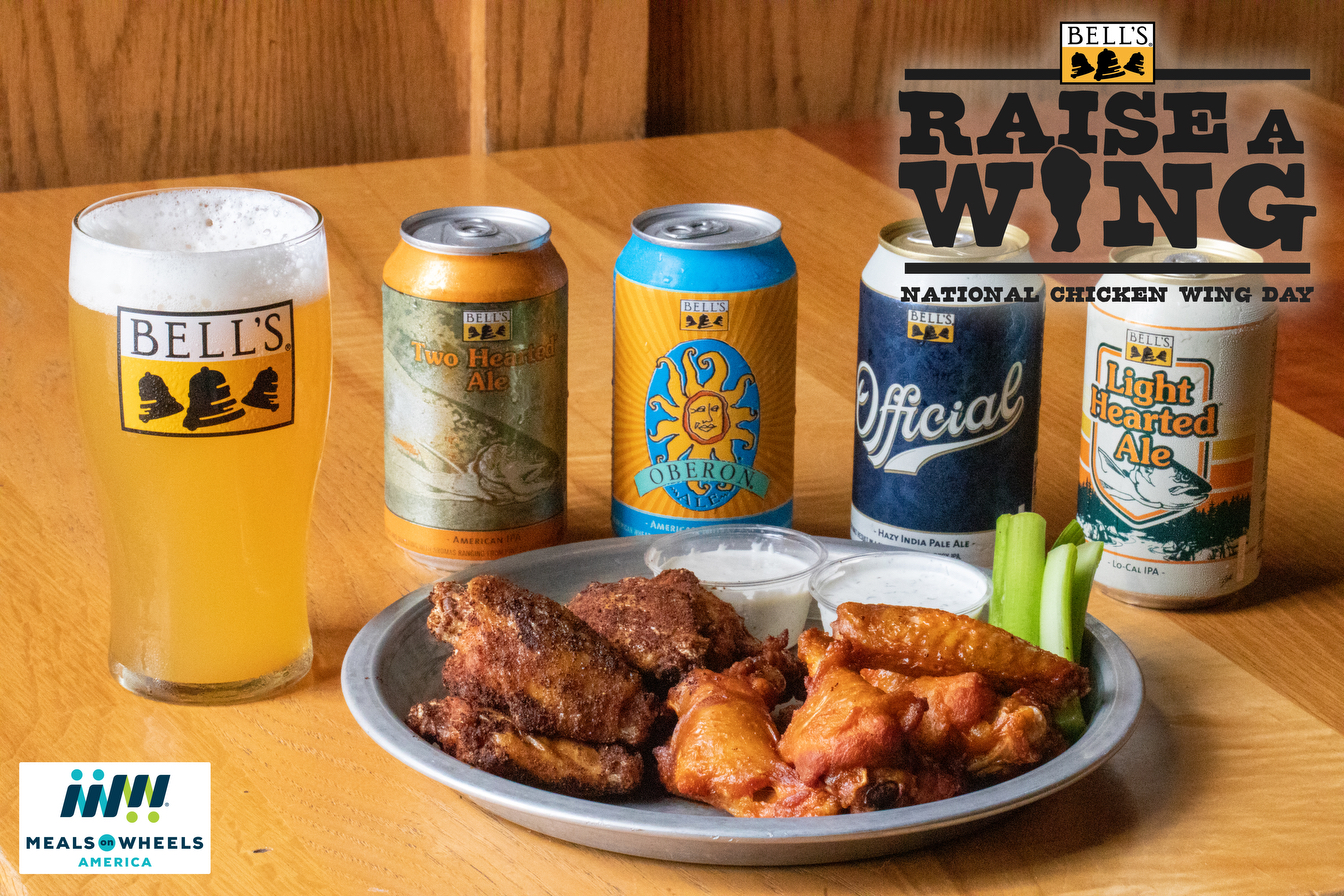 A plate of chicken wings in front of a line up of Bell's beer cans, including Two Hearted, Oberon, Official and Light Hearted, next to a golden pint of beer in a glass with the Bell's logo