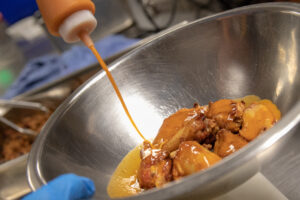 Two Hearted buffalo sauce being poured onto chicken wings in a bowl