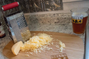 a cutting board with a cheese grater and grated cheese