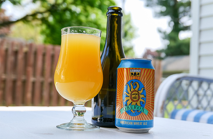 A can of Oberon next to a Champagne bottle next to a glass of orange liquid
