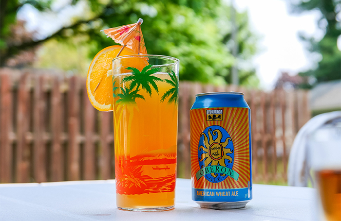 A can of Oberon next to a tropical decorated glass with orange liquid.
