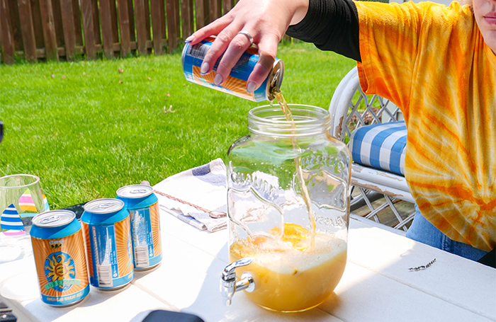 A large pitcher with fruit inside and pouring cans of Oberon into it