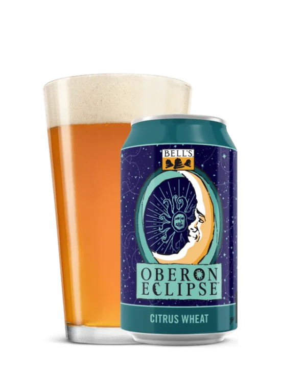 A can with a blue starry sky design behind a logo of a crescent moon inside of the oberon sun face and the words oberon eclipse, behind it is a glass filled with the beer