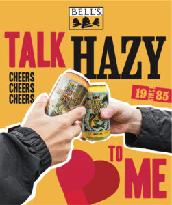 Two hands clinking cans of Bell's Two Hearted IPA and Hazy Hearted IPA with a heart in the background and the words "TALK HAZY TO ME" in bold font.