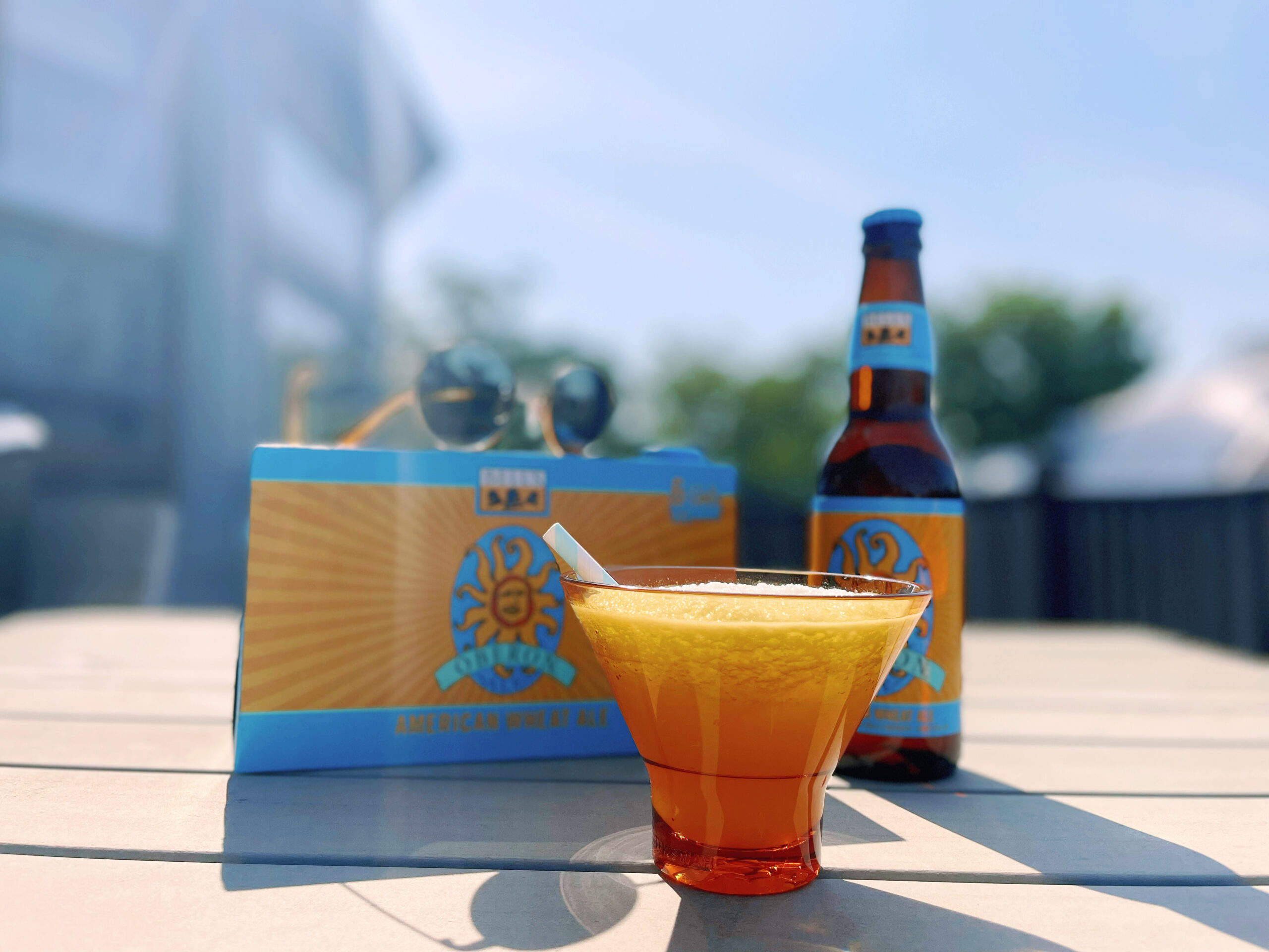 Oberon slush cocktail in a low-ball glass on a deck outside. In the background, there’s a bottle of Oberon and a 6-pack of cans.